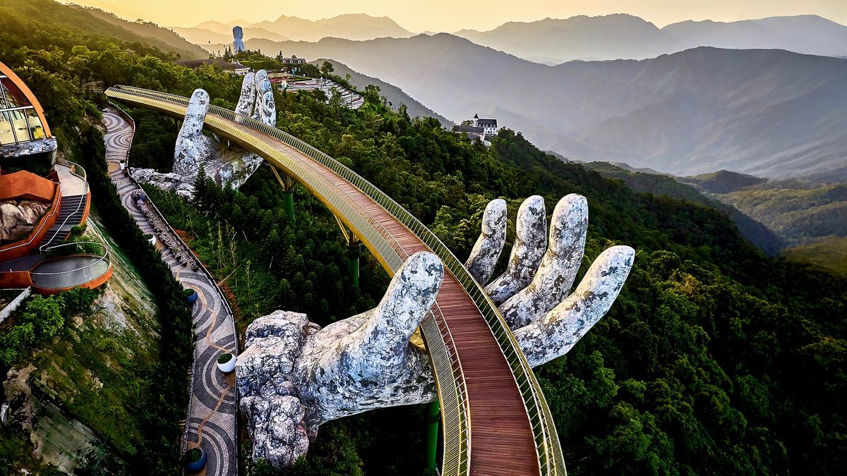 Cầu Vàng nhìn từ trên cao, dải cầu uốn cong giữa rừng và dãy núi phía sau