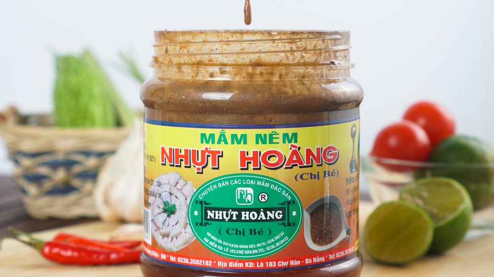 Hũ mắm nêm Nhựt Hoàng đặt trên thớt gỗ cùng tỏi, ớt và chanh